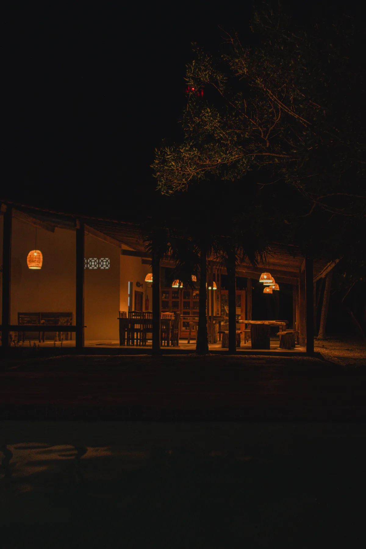 Espaço de convivência da NAK iluminado durante a noite, com mesas compartilhadas e ambiente integrado em meio à natureza.