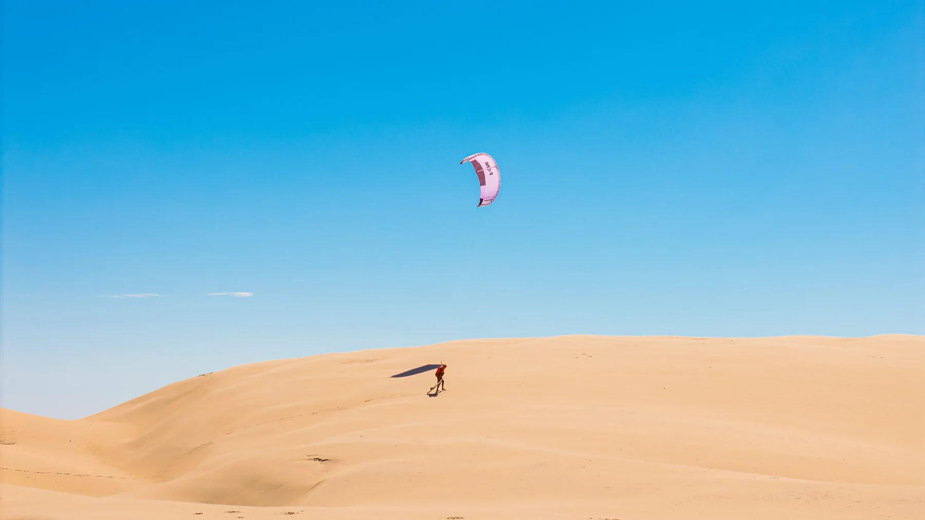 Kitesurfista caminhando pelas dunas dos Lençóis Maranhenses com a pipa inflada ao vento.
